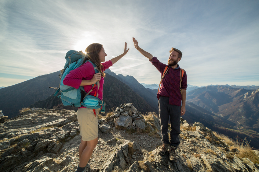 Couple of hikers reaches mountain top, celebrates with high five.
