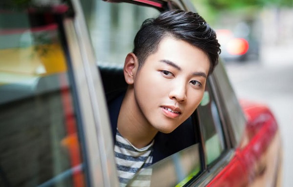 Handsome well-dressed young asian man is looking out of the red taxi rear window and observing the life on the street and where he is going. The image is colourful and bright. The model is looking sharp and extremely youthful. Image contains some copy space. Made in Hong Kong, China.