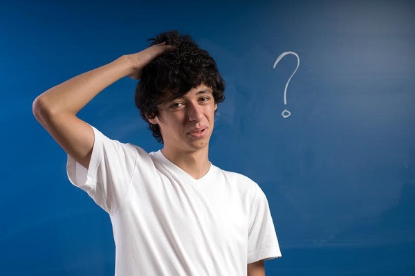Young Man Scratching Head in Front of Blackboard