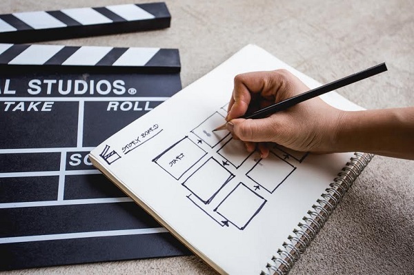 hand with holding pencil for writing  storyboard in sketchbook beside clapperboard